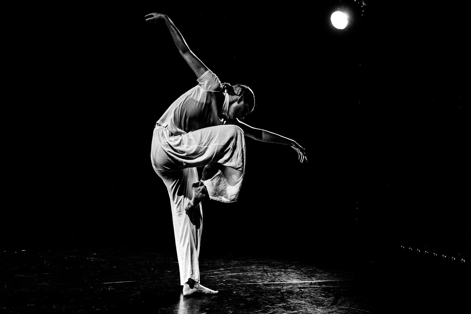 A dancer performs gracefully on a dark stage.